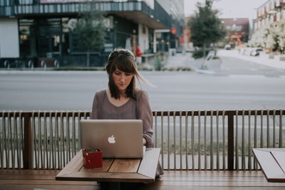 穿着灰色衬衫的女人坐在MacBook前的长凳上